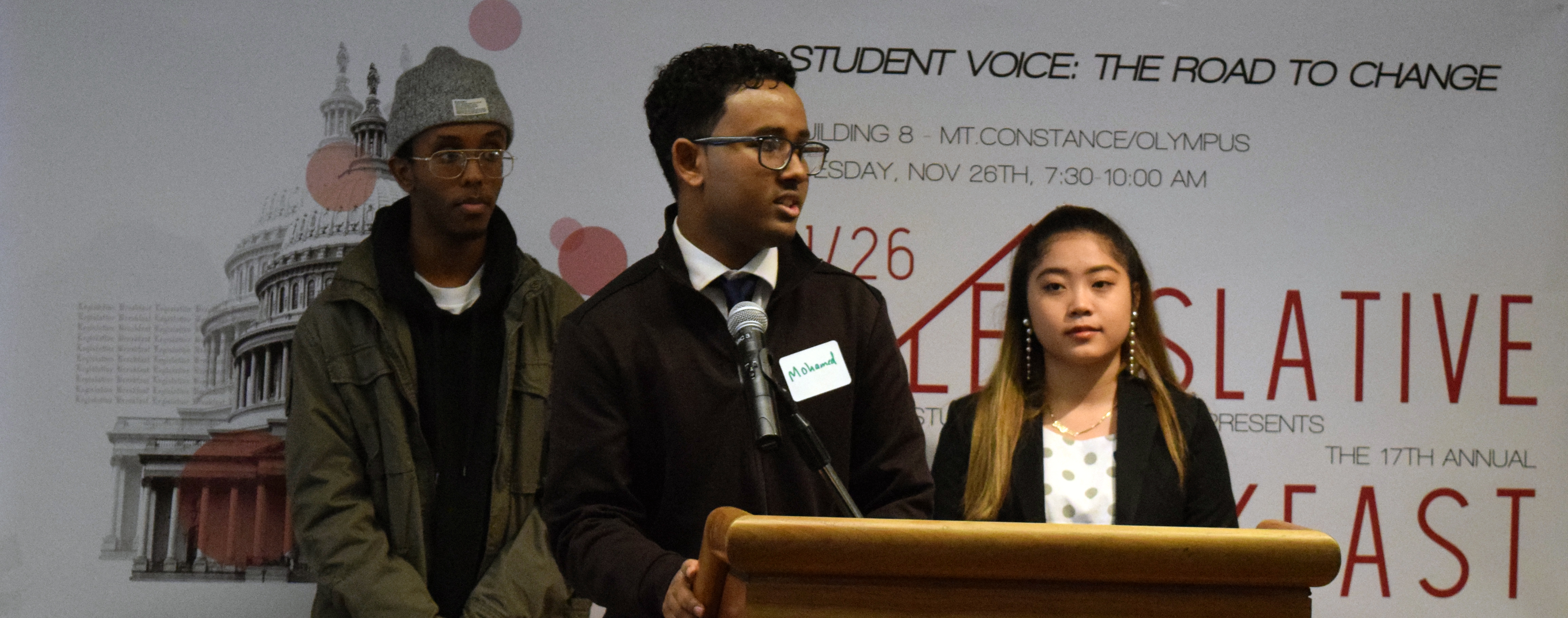 Student government leaders stand at a podium with "Legislative Breakfast" banner behind them